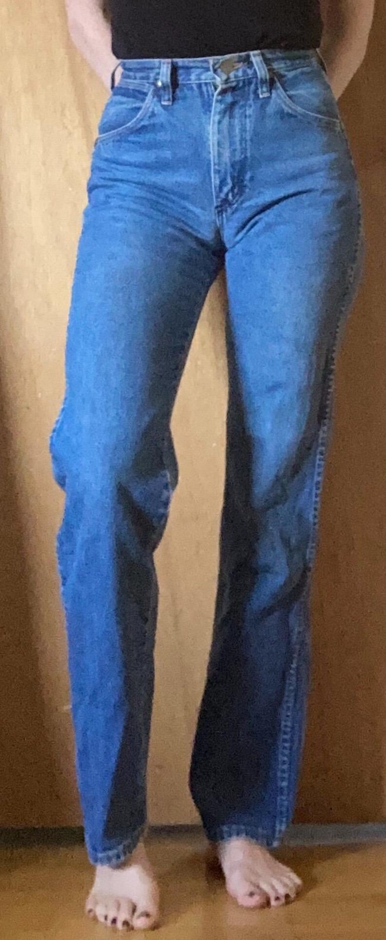 May include: High-waisted blue denim jeans featuring a classic five-pocket design, a metal button closure at the waistband, and a straight-leg cut. The denim has a medium blue wash with subtle fading along the thighs and seams, finished with a standard hem.