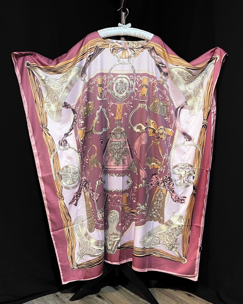 May include: A pink silk robe with a gold and white print of equestrian themed designs. The robe has a wide, flowing silhouette and a relaxed fit.