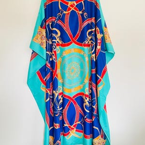May include: A turquoise blue maxi dress with a colorful print of red, blue, and gold chains and belts. The dress has a round neckline and a loose, flowing silhouette.