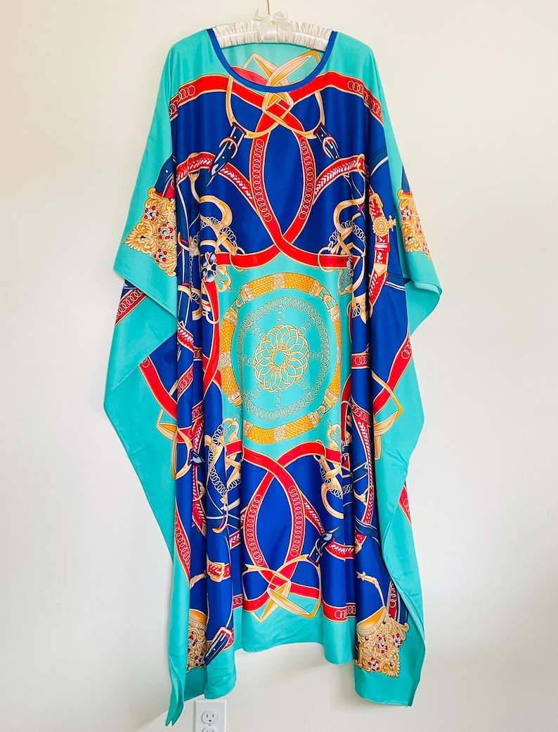 May include: A turquoise blue maxi dress with a colorful print of red, blue, and gold chains and belts. The dress has a round neckline and a loose, flowing silhouette.