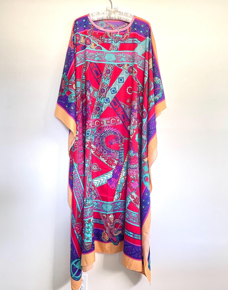 May include: A long, flowing, pink and purple kaftan with a colorful geometric pattern of belts, buckles, and other designs. The kaftan has a round neckline and a relaxed fit.