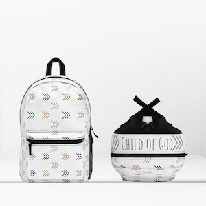 Puede incluir: Una mochila blanca y una bolsa de cordón blanca con una correa negra. Ambas tienen un patrón de flechas negras, doradas y grises. La bolsa de cordón tiene el texto "CHILD OF GOD" en negro.