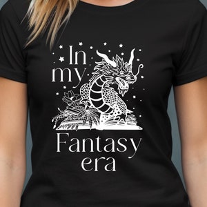 May include: Black t-shirt with a white graphic of a dragon curled around an open book. The text "In my Fantasy era" is printed below the dragon.