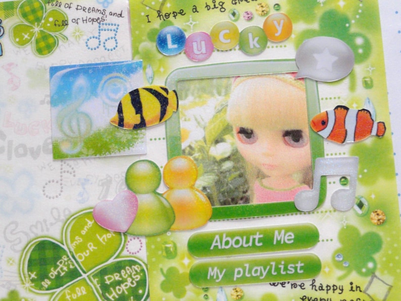 May include: A scrapbook page with a green and white theme, featuring a photo of a doll, fish stickers, and the word "Lucky". Decorative elements include musical notes, clovers, and text that reads "About Me" and "My playlist".