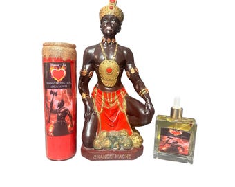 May include: A red candle with gold glitter, a statue of a kneeling figure with a red and gold outfit, and a clear bottle of oil with a red and gold label. The candle label says "Blessings of Joy" and "Mango Protection, Love & Money". The statue is labeled "Changó Macho". The oil label says "Blessings of Joy" and "Mango Protection, Love & Money".