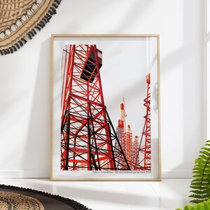 May include: A framed art print showcasing a red and black architectural illustration of towers on a white backdrop. The artwork, titled "Yakov Chernikhov - 60 Arkhitekturnye fantazi 1933", is presented in a wooden frame, suitable for wall display.