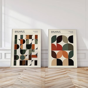 Può includere: Due stampe artistiche Bauhaus incorniciate. La stampa a sinistra presenta forme geometriche marroni, verdi e nere. La stampa a destra ha un design simile con forme rosse, verdi e nere. Entrambe le stampe hanno la parola "BAUHAUS" in alto.