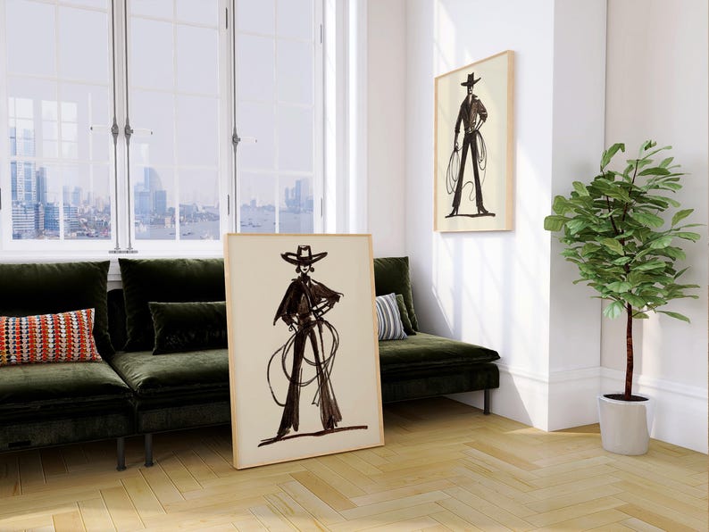 Pu&ograve; includere: Due stampe artistiche incorniciate raffiguranti un'illustrazione in bianco e nero di una persona con cappello e abiti da cowboy. Una stampa &egrave; appoggiata a un muro, l'altra &egrave; appesa. La stanza comprende un divano verde e una pianta.