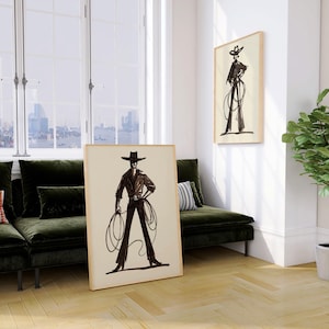 Pu&ograve; includere: Due stampe artistiche incorniciate raffiguranti un bozzetto in bianco e nero di un cowboy con un lazo. Una stampa &egrave; appoggiata a un muro, l'altra &egrave; appesa. La stanza ha un divano in velluto verde, una pianta in vaso e una vista sulla citt&agrave; attraverso una grande finestra.