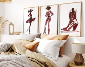 May include: Three framed art prints with a fashion theme. The prints feature sketches of a woman in a dress, a woman in a pantsuit, and a cowboy boot. The artwork is in shades of red and brown, set against a white background.