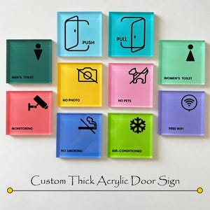 Può includere: Una collezione di cartelli per porte quadrati in acrilico colorato con varie icone e testo, tra cui "PUSH", "PULL", "MEN'S TOILET", "WOMEN'S TOILET", "NO PHOTO", "NO PETS", "NO SMOKING", "AIR-CONDITIONED", "MONITORING" e "FREE WIFI". È presente anche il testo "Custom Thick Acrylic Door Sign".