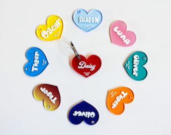 May include: Assortment of colorful heart-shaped pet ID tags with white lettering. The tags feature names like Tiger, Daisy, Oliver, and Luna.