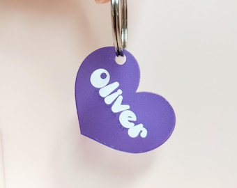 May include: Purple heart-shaped tag with a silver key ring. The tag has the name "Olivers" printed in white.
