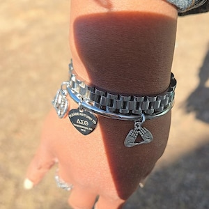 May include: A silver bracelet with a charm that says "Please Return to Delta Sigma Theta 1913" and another charm with two hands forming a triangle.