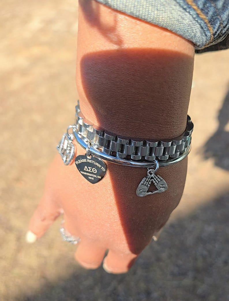 May include: A silver bracelet with a charm that says "Please Return to Delta Sigma Theta 1913" and another charm with two hands forming a triangle.