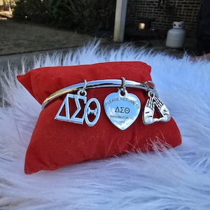 May include: Silver charm bracelet with a heart charm that says "Please return to Delta Sigma Theta Washington, DC 1913" and other charms including a Greek letter charm and a charm with two hands clasped in prayer.