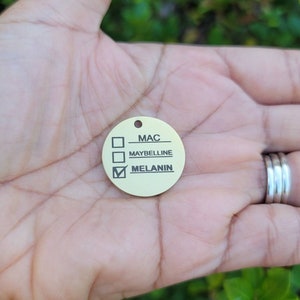 May include: A gold-colored round tag with a checklist. The options are MAC, Maybelline, and Melanin. The box next to Melanin is checked.