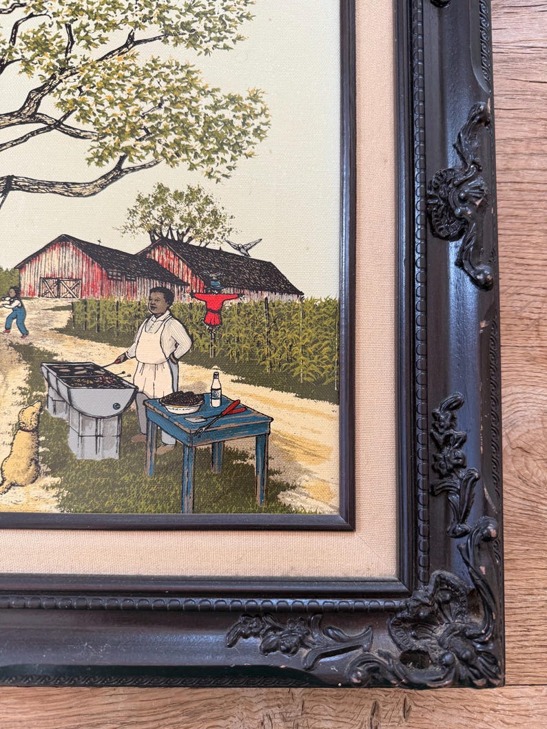 Peut inclure: Une peinture encadr&eacute;e repr&eacute;sentant une sc&egrave;ne rurale avec un homme faisant griller des aliments sur un barbecue au charbon de bois. Il y a deux granges rouges en arri&egrave;re-plan, un &eacute;pouvantail et un arbre. La peinture est dans un cadre brun fonc&eacute; avec des d&eacute;tails orn&eacute;s.