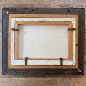Peut inclure: L'arri&egrave;re d'une peinture encadr&eacute;e avec un cadre en bois. Le cadre est brun fonc&eacute; avec un cadre int&eacute;rieur brun plus clair. La toile est blanche et comporte quelques agrafes qui la maintiennent en place.