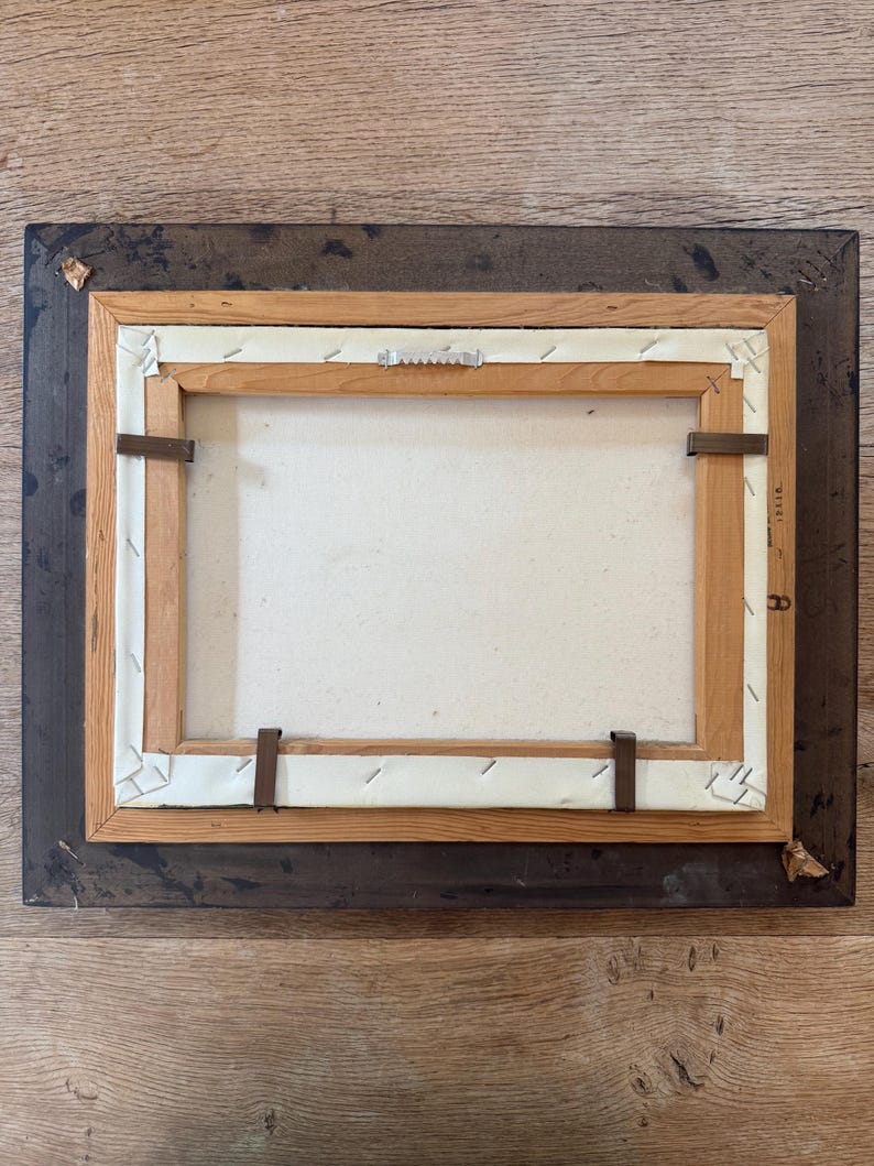 Peut inclure: L'arri&egrave;re d'une peinture encadr&eacute;e avec un cadre en bois. Le cadre est brun fonc&eacute; avec un cadre int&eacute;rieur brun plus clair. La toile est blanche et comporte quelques agrafes qui la maintiennent en place.