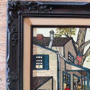 Peut inclure: Une peinture encadr&eacute;e repr&eacute;sentant une maison blanche avec un toit bleu et un porche. La maison a une chemin&eacute;e en brique rouge et une porte bleue. Deux personnes sont assises sur la balan&ccedil;oire du porche, et une troisi&egrave;me personne est debout sur le porche. La peinture est sur fond de verdure et de ciel bleu.