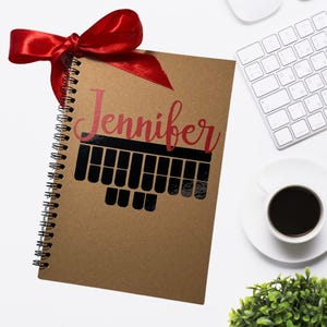May include: A brown spiral notebook with a red ribbon and the name "Jennifer" printed in red on the cover. A black keyboard graphic is printed below the name.
