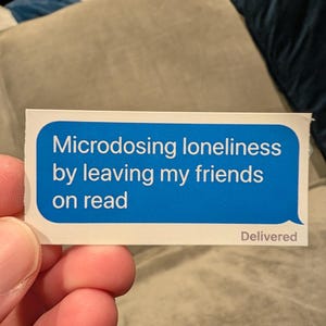 Op de afbeelding: Een rechthoekige sticker in de vorm van een blauwe digitale berichtballon met witte tekst: Microdosing loneliness by leaving my friends on read. In de rechterbenedenhoek van de sticker staat de kleine grijze tekst: Delivered.