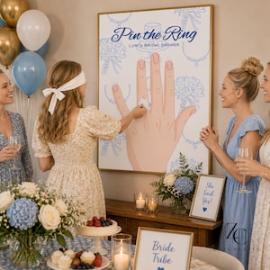 Puede incluir: Un juego de despedida de soltera con el texto "Pin the Ring" en un póster grande. Cuatro mujeres se reúnen, una con los ojos vendados, intentando colocar un anillo en una ilustración de una mano. Globos y arreglos florales decoran la habitación.