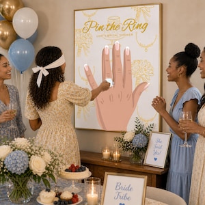 Puede incluir: Un juego de despedida de soltera con un póster que dice "Pin the Ring". El póster presenta una ilustración de una mano con un anillo que se va a colocar en un dedo. Varias mujeres se reúnen, algunas sosteniendo bebidas, con globos y arreglos florales en el fondo.