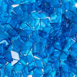 May include: A pile of small, translucent, blue glass tiles. The tiles are various shapes and sizes, and they are scattered randomly.