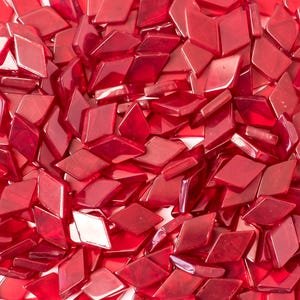 Op de afbeelding: Een close-up van talrijke kleine, ruitvormige, doorschijnende rode glazen tegels. De tegels zijn verspreid, waardoor een textuur ontstaat. De glanzende afwerking reflecteert het licht en benadrukt de rijke rode kleur en de facetten van elke tegel.