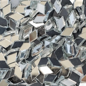 May include: A collection of small, diamond-shaped glass tiles in various shades of silver, black, and clear. The tiles are scattered, creating a textured surface. Ideal for mosaic projects or decorative crafts.