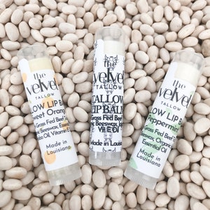 May include: Three white tubes of lip balm with green and white labels. The labels have the text "the velvet tallow" and list the flavors "Sweet Orange", "Peppermint", and "Tallow Lip Balm".