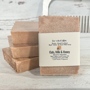 May include: A stack of four brown bars of soap with a white label that reads "the velvet tallow Rustic, Hand-Crafted Beef Tallow & Goat Milk Soap Oats, Milk & Honey Elements: Saponified Beef Tallow, Lard, Castor Oil Colloidal Oats, Goat Milk, Local Honey, Fragrance"