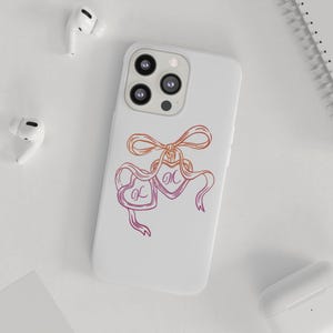 May include: White phone case featuring a heart-shaped design with the letters "L" and "M" on ribbons, accented with a bow. The design is in shades of orange and pink. The phone case has a triple-lens camera.