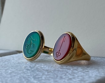 May include: Two gold signet rings with oval shaped green and red gemstones. The green stone has the initials "F.G." engraved on it. The red stone has a key engraved on it.