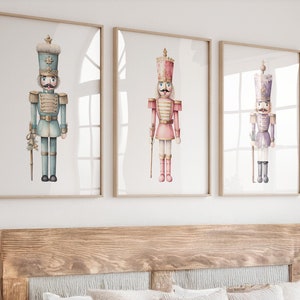 Puede incluir: Tres acuarelas de soldados cascanueces. El primer cascanueces lleva un uniforme azul y dorado, el segundo lleva un uniforme rosa y dorado, y el tercero lleva un uniforme morado y dorado.