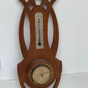 May include: A wall-mounted weather station featuring a brown wooden frame with geometric cutouts. It includes a vertical thermometer with a Centigrade scale and a round barometer with a brass-colored rim and a dial displaying weather conditions.