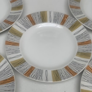 May include: A set of white ceramic plates with a mid-century modern design. The plates feature a white center and a rim with a pattern of black, orange, and olive green lines radiating outwards.