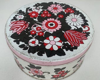 May include: A round, vintage tin with a floral design. The lid features a pattern of red, pink, and white flowers with black leaves on a white background. The sides are white with a pink band and repeating floral pattern.