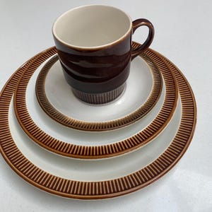 May include: A set of three brown and white ceramic plates with a brown rim and a brown and white ceramic mug.