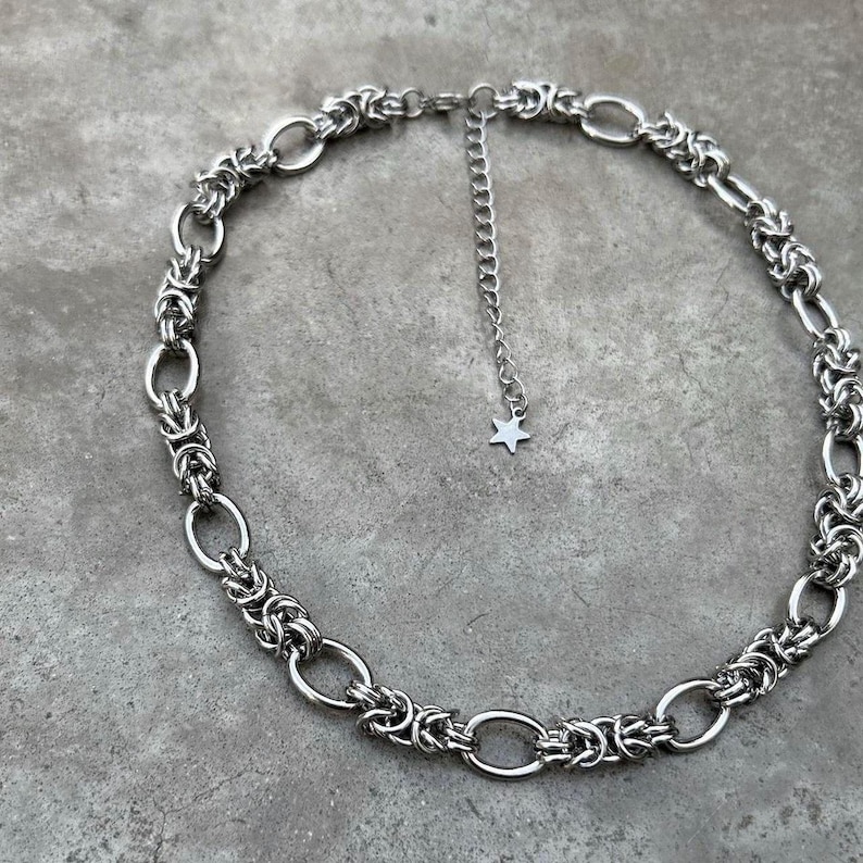 May include: A silver chain necklace with a star charm. The chain is made of interlocking oval links.