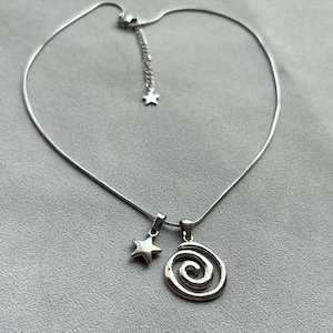 May include: A silver chain necklace with a star and a spiral pendant. The necklace is on a gray background.