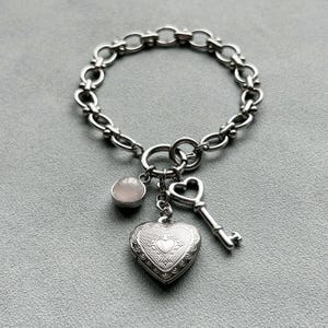May include: A silver chain bracelet with a heart-shaped locket, a small key charm, and a clear stone charm.