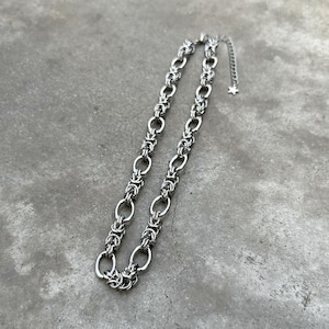 May include: A silver chain necklace with a delicate, intricate design. The chain is made of small, linked rings that create a woven pattern.