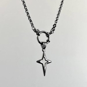 Silver-toned necklace featuring a star pendant. The pendant has a four-pointed star design with a hollow center. The necklace has a chain with a large ring clasp. The jewelry is set against a white background.