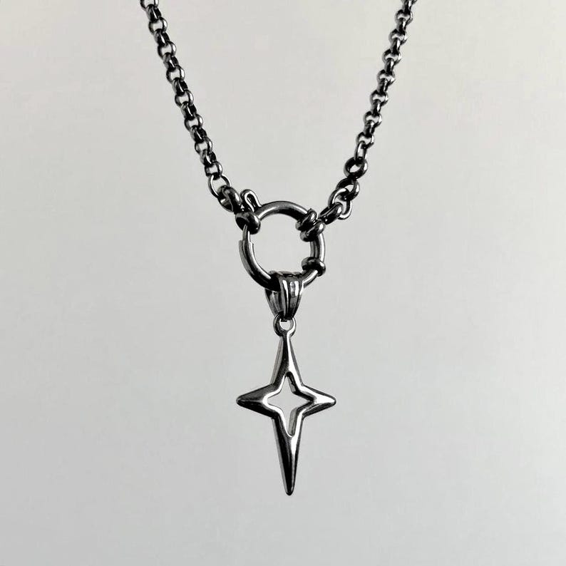 Silver-toned necklace featuring a star pendant. The pendant has a four-pointed star design with a hollow center. The necklace has a chain with a large ring clasp. The jewelry is set against a white background.