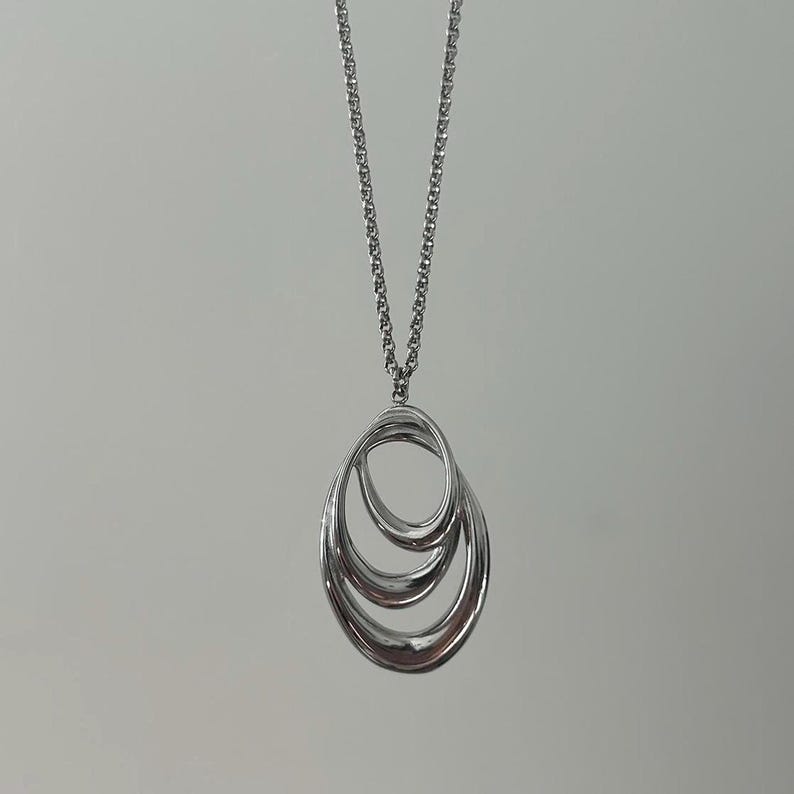 May include: A silver necklace with a pendant featuring three interlocking oval shapes.
