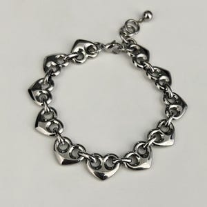 May include: A silver-toned bracelet featuring heart-shaped links. The bracelet has a delicate chain design with a lobster clasp closure and an adjustable extension chain. The hearts are evenly spaced and connected by small circular links, creating a romantic and stylish accessory.