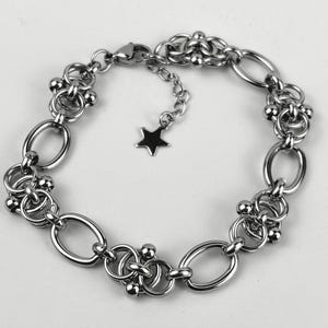 May include: A silver-toned chain bracelet featuring alternating oval links and intricate circular clusters accented with small spheres. The bracelet includes an adjustable chain extension finished with a small, flat, five-pointed star charm.